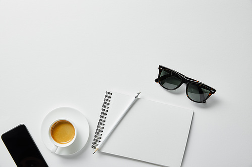 top view of coffee, notebook, pencil and glasses with smartphone on white surface