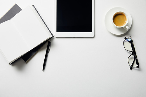 top view of digital tablet, coffee, glasses and notebooks with pen on white surface