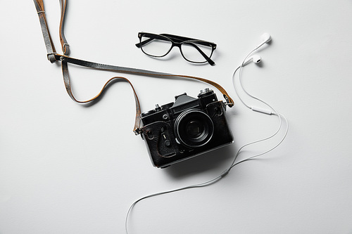 top view of earphones, glasses and photo camera on white surface