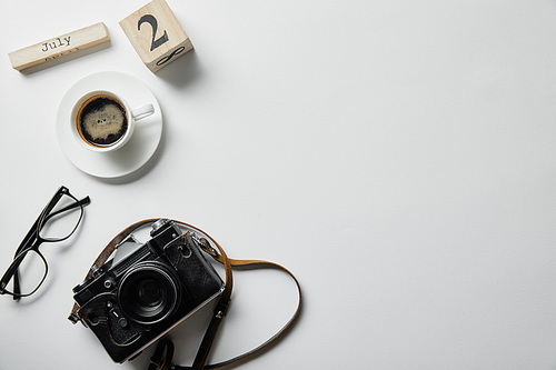 top view of photo camera, glasses, coffee, block with numbers and letters on white surface