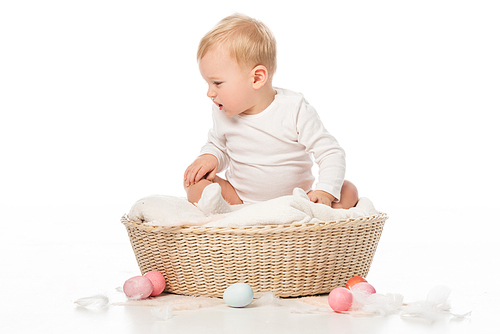 child looking down and sitting in basket with . eggs around on white background