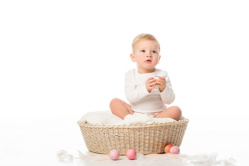 child holding . egg, sitting in basket with colorful decoration around on white background