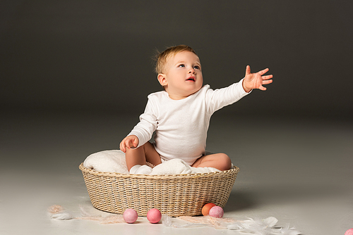 Child with outstretched hand looking up, sitting in basket on black background