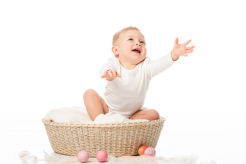 Cute child with outstretched hands and open mouth sitting in basket on white background