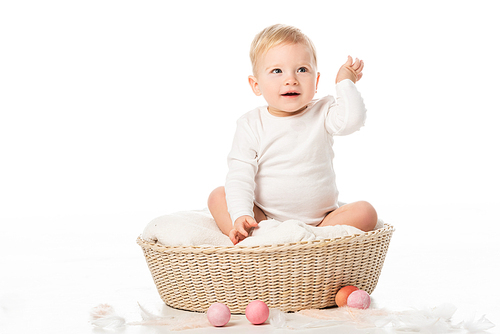child with raised hand sitting on blanket in basket with . eggs around on white background