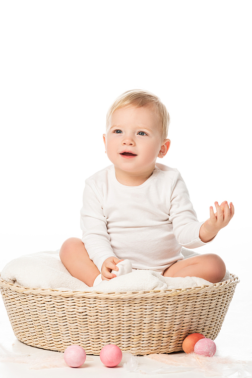 child with raised hand sitting in basket with . eggs around on white background