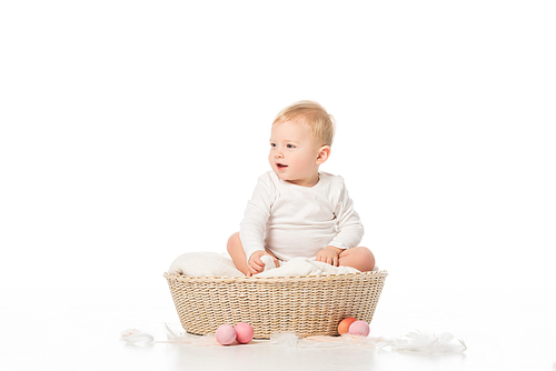 child with open mouth looking away, sitting in basket next to . eggs on white background