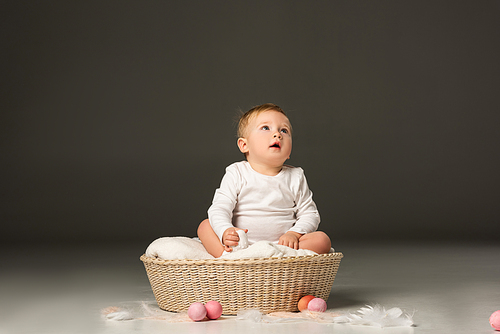 cute child holding . egg, looking up with open mouth in basket on black background