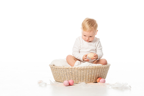 child with lowered head holding . egg, sitting on blanket in basket on white background