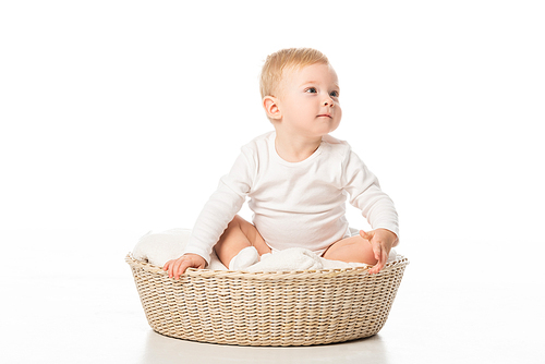 Cute child looking away and sitting on blanket in basket on white background