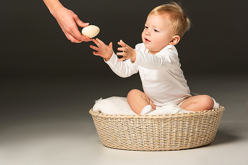 cropped view of cute boy taking . egg from woman hand, sitting on blanket in basket on black background
