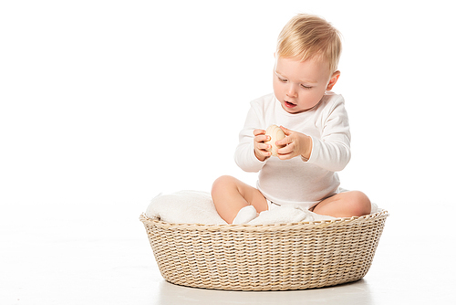 child looking at . egg in hands with open mouth in basket on white background