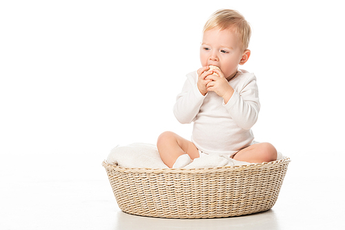 child taking . egg to mouth by clenched hands, sitting on blanket in basket on white background