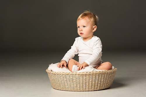 Cute boy sitting on blanket in basket on black background