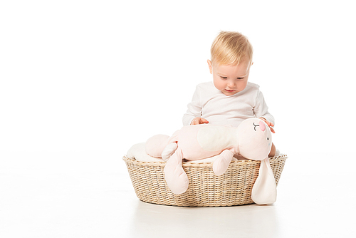 Child looking at pink bunny and sitting on blanket in basket on white background