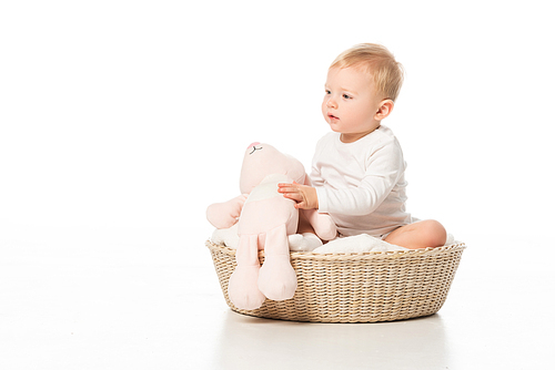 Cute child holding pink bunny and sitting on blanket in basket on white background