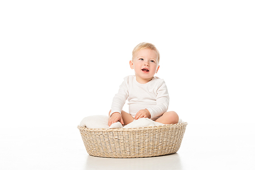 Cute boy with open mouth sitting on blanket in basket on white background