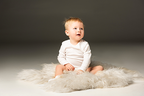 Cute child looking away with open mouth, sitting on fur on black background