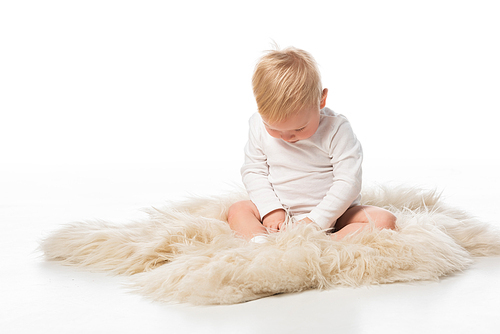 Cute child with lowered head sitting on fur on white background