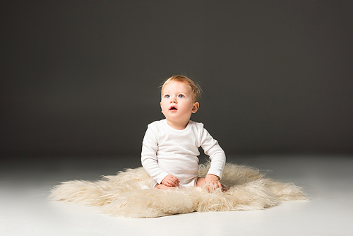 Cute kid looking up with open mouth, sitting on fur on black background