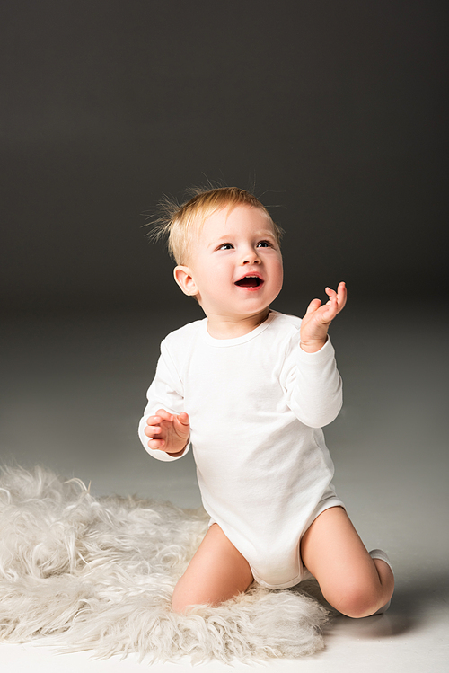 Cute happy kid looking up with open mouth, sitting on fur on black background