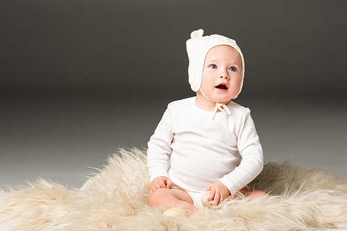 child wearing baby bonnet, holding . egg with open mouth on fur on black background