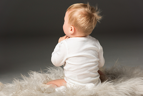 Back view of cute kid sitting on fur on isolated on black