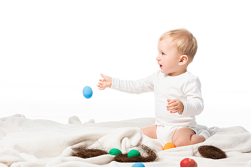 Child throwing easter egg while sitting on blanket isolated on white