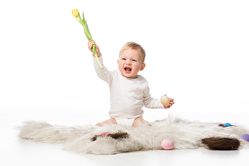 child with open mouth holding tulip and . egg, sitting on fur on white background