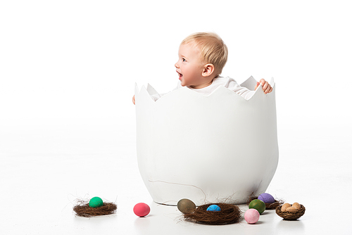 cute child looking away in eggshell with nests and . eggs around on white background