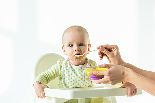 Mother feeding baby on feeding chair with baby nutrition on white background