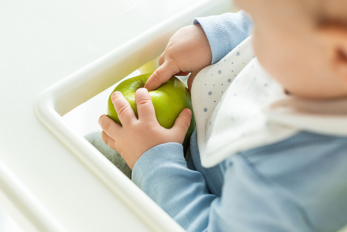 Selective focus of baby touching green apple on feeding chair isolated on white