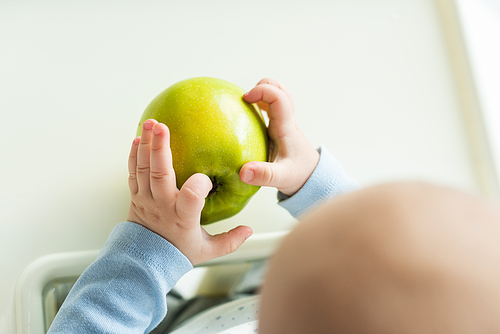 Overhead view of baby holding green apple while sitting on feeding chair