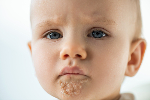 Portrait of sad baby boy with puree on soiled mouth isolated on grey