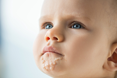 Portrait of cute infant with soiled mouth with baby food isolated on grey