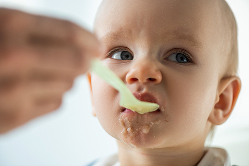 Selective focus of mother feeding baby with puree on grey background