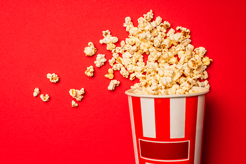 Top view of bucket with tasty popcorn on red background