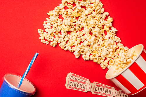 Top view of popcorn, cinema tickets and paper cup on red surface