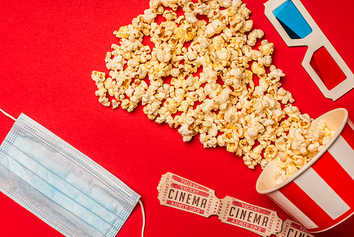 Top view of medical mask, cinema tickets with popcorn and 3d glasses on red background