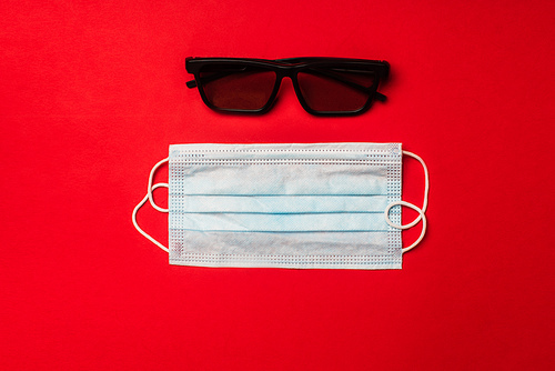 Top view of medical mask and sunglasses on red background