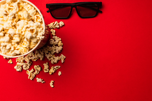 Top view of sunglasses near bucket with tasty popcorn on red background