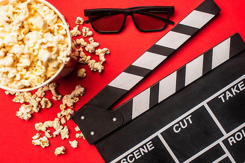 Top view of clapperboard near bucket with popcorn ans sunglasses on red background