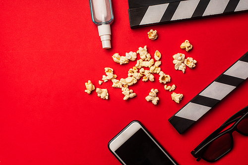 Top view of smartphone near clapperboard, popcorn and hand sanitizer on red background
