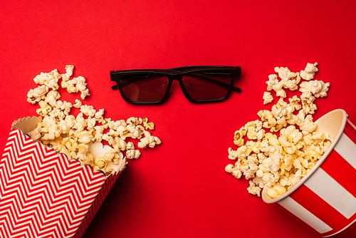 Top view of sunglasses near buckets with popcorn on red background