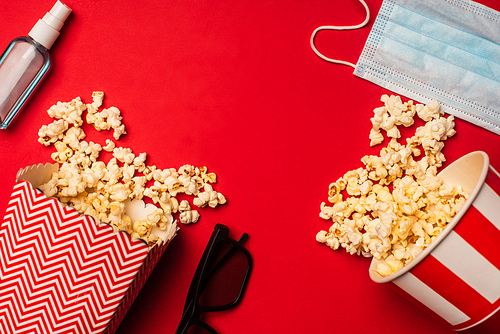 Top view of popcorn, medical mask with hand sanitizer and sunglasses on red background