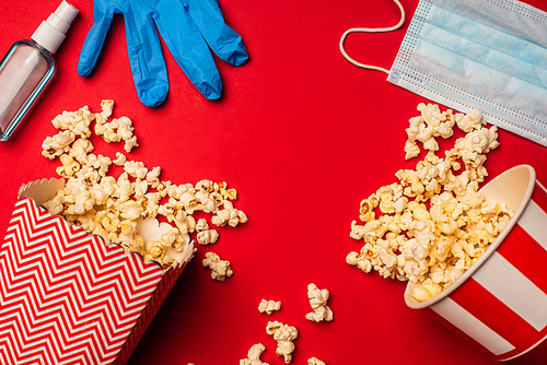 Top view of latex glove near medical mask, popcorn and hand sanitizer on red background