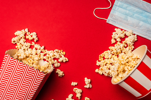 Top view of buckets with popcorn and medical mask on red background