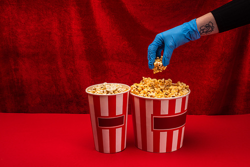 Cropped view of woman in latex glove holding popcorn on red surface with velour at background
