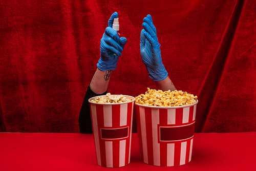 Cropped view of popcorn near woman in latex gloves holding hand sanitizer on red surface with velour at background