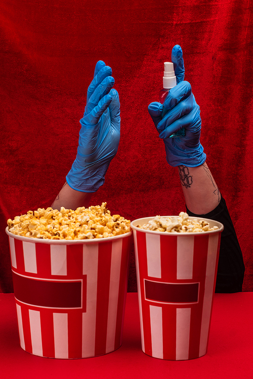 Cropped view of popcorn near girl in latex gloves using hand sanitizer on red surface with velour at background